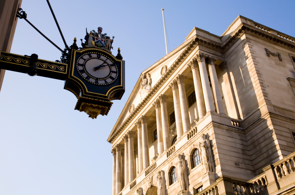 Bank of England building with blue sky behind it and a decorative clock next to it.